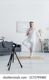 Senior Yoga Coach Showing Tree Pose And Prana Mudra Gesture In Front Of Digital Camera