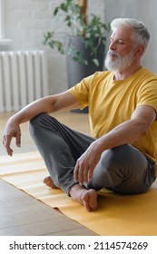 senior yoga, a man with gray hair meditates and does breathing exercises. sports fitness and physical exercises for the elderly. a fifty-year-old European man holds his hands in namaste in a yellow T