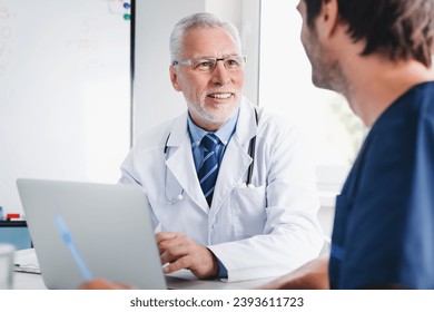 Senior and young doctors having informal meeting in clinic. Doctors talking about difficult diagnosis, collecting data about medical patient`s history - Powered by Shutterstock