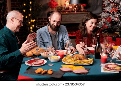 Senior and young people on christmas eve gathering at table to eat homemade food and drink wine, being festive together. Diverse family and friends having fun celebrating december holiday. - Powered by Shutterstock