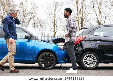 Senior and younger male drivers get out of cars and inspect damage after road traffic accident