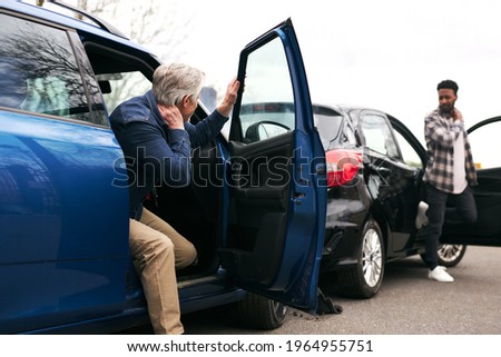 Senior and younger male drivers get out of cars and inspect damage after road traffic accident