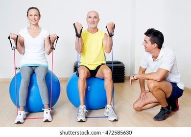 Seniors Doing Biceps Curl On A Medicine Ball With Personal Trainer