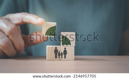 senior's hand complete umbrella over family icon on wooden cube blocks, for life or group insurance
