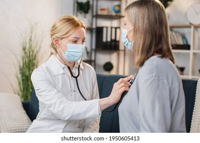 Seniors heart diseases, cardiology concept. Female blond physician in mask holding stethoscope and listening retired woman during homecare visit. Doctor checking heartbeat of senior woman at home - Powered by Shutterstock