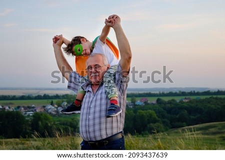 Senor man rolls on the shoulders of his little grandson. a little boy imagines that he is flying like a hero. fun family trips.