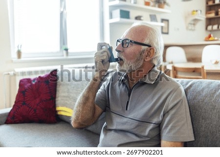 Senor using asthma inhaler to relief an attack. Man using asthma inhaler for preventing attack. Mature man using medical inhaler to prevent and treat wheezing and shortness of breath caused by allergy