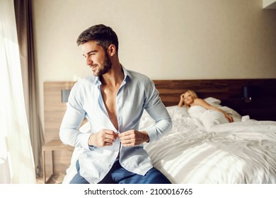 Sensations Morning After A Night Spent Making Love. A Love Affair Between Two Lovers In A Hotel Room. The Man Gets Dressed And Fastens The Shirt Button While The Woman Is Still Lying Naked In Bed