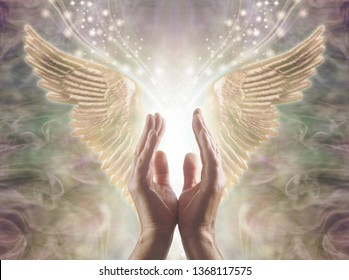 Sensing Angelic Energy - Male hands reaching up into a beautiful pair of golden Angel wings with white light and sparkles flowing  between, against a warm ethereal energy formation background
