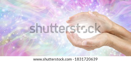Sensing Awesome Metaphysical Energy Field between hands - female cupped hands with white healing energy against a colourful blue purple green sparkling chaotic background with copy space 
