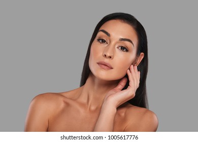 Sensitive Care For A Luminous Skin. Attractive Young Woman Looking At Camera While Standing Against Grey Background