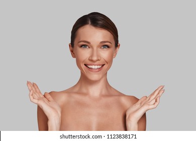 Sensitive Care For A Luminous Skin. Attractive Young Woman Looking At Camera And Smiling While Standing Against Grey Background