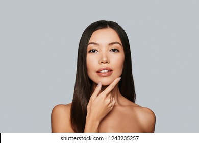 Sensitive Care For A Luminous Skin. Beautiful Young Asian Woman Looking At Camera And Smiling While Standing Against Grey Background