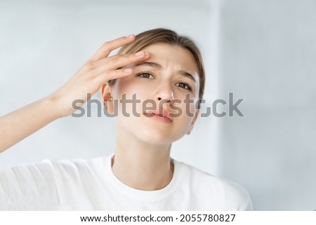 Sensitive skin. Acne problem. Zit treatment. Frustrated young woman touching itchy dry face wrinkle on white defocused background.