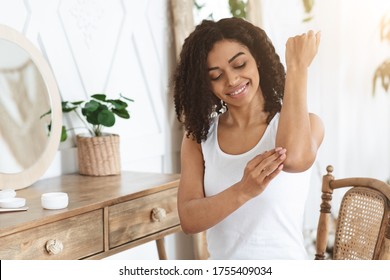 Sensitive Skin Treatment. Cheerful Afro Woman Applying Moisturising Soothing Cream At Elbow Zone, Pampering Herself At Home, Free Space