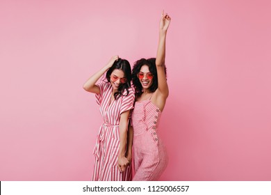 Sensual african lady having fun with her best friend. Indoor photo of adorable girls in pink clothes standing on light background.
