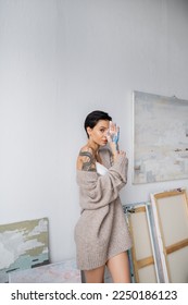 Sensual artist covering face with hand in paint in workshop - Shutterstock ID 2250186123