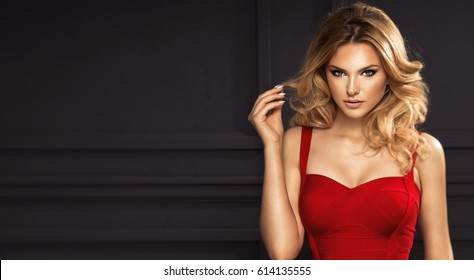 Sensual beautiful blonde woman posing in red dress. Girl with long curly hair.