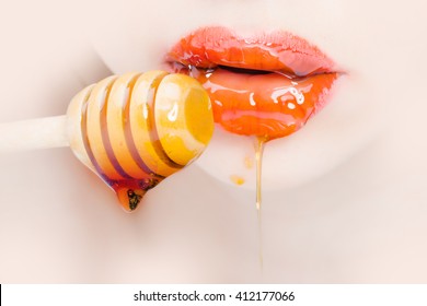 Sensual female red lips eating honey from wooden spoon closeup