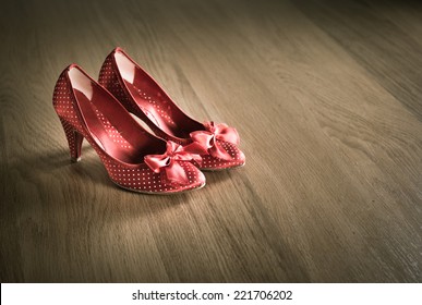 Sensual red female shoes on hardwood floor with ribbon and dotted texture.