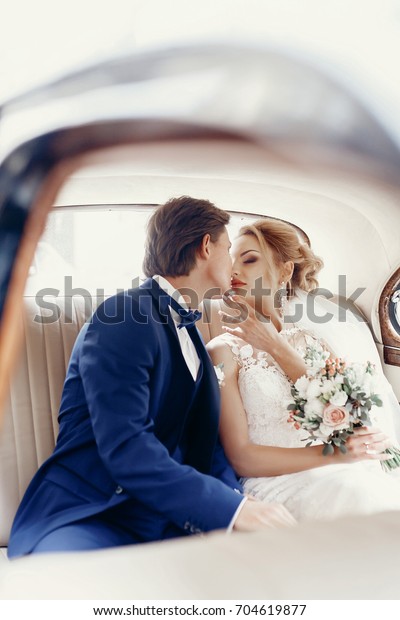 Sensual wedding\
couple - bride and groom kissing in luxury car before wedding\
ceremony mirror reflection, stylish groom in blue suit kissing with\
blonde bride with\
bouquet