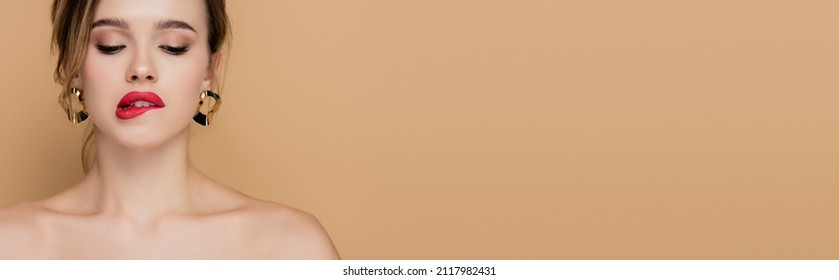 sensual woman with naked shoulders biting lip isolated on beige, banner