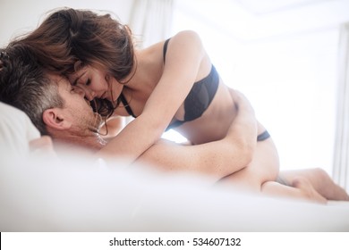 Sensual young couple making love in bedroom. Beautiful woman in underwear on top of man lying on bed.