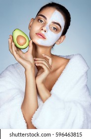 Sensual young girl holding half an avocado in hand. Photo of beautiful girl with moisturizing facial mask. Beauty & Skin care concept