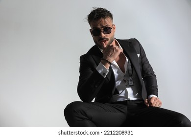 Sensual Young Groom In Tuxedo With Open Collar Shirt Touching Lips In A Seductive Manner In Front Of Grey Background In Studio