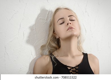 sensual young woman with closed eyes near white wall background
