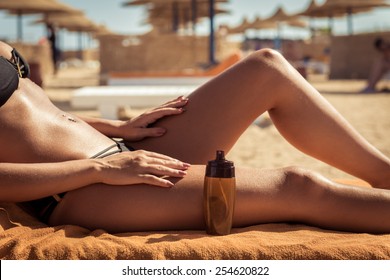Sensuous slim woman applying suntan lotion oil to her body at the beach