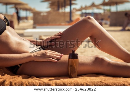 Sensuous slim woman applying suntan lotion oil to her body at the beach