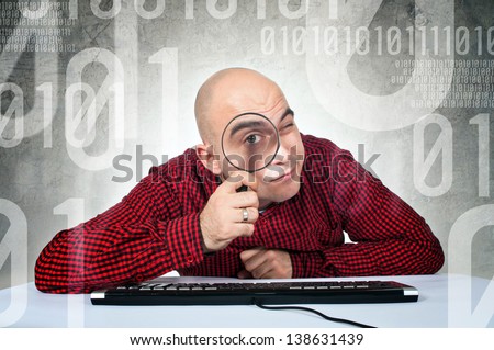 SEO engineer or computer search concept. Man sitting at the computer table with keyboard holding magnifying glass.