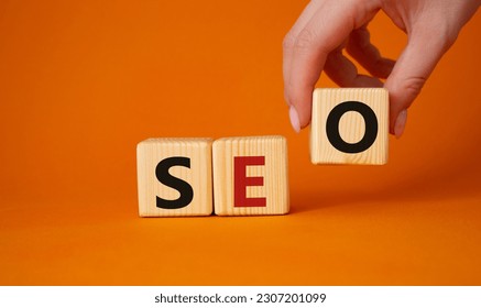 SEO - Search Engine Optimization symbol. Wooden blocks with words SEO. Businessman hand. Beautiful orange background. Business and SEO concept. Copy space.