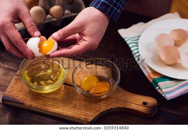 Separated eggs over dark brown wooden table.\
Man separating the yolk from the egg\
white.