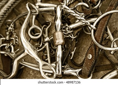 Sepia tinted close-up of a pile of well-used horse bits, tack leather and a rope (shallow depth of field).