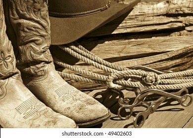 Sepia-toned rustic western image of cowboy boots, cowboy hat, rope, horse bits and stacked wood.