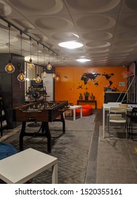 SEPT. 19, 2019-SEOUL KOREA: A Room With A Drawing Of The World Map On An Orange Painted Wall. Foosball Table, Tables, Chairs And Desk In A Room. Game Room With Cool Lighting. Office Game Room Concept.