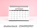 September 2025 desk calendar on white table with pink color background.