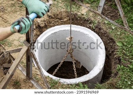Septic Tank or Well Installing for Country House. Septic Well Concrete Rings Laying Undeground by Worker Hands. Construction of Sewer Well.