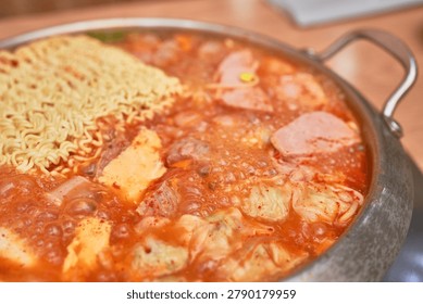      A sequential visual narrative of Budae-jjigae, a popular Korean spicy sausage stew, served in a shallow stainless steel pot. The first image displays a rich red broth generously loaded with spam, sausages, mini dumplings, rice cakes, and a slice of yellow cheese. The second image shows the addition of a classic block of instant ramen noodles. The final close-up captures the stew actively boiling, with the cheese melting into the bubbling spicy broth. This collection perfectly highlights the dynamic, hearty, and savory essence of this beloved Korean comfort food.                          