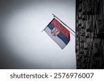 The Serbian flag waves in front of a gray sky over Belgrade. The national emblem’s bold red, blue, and white colors stand out against the subdued urban backdrop.