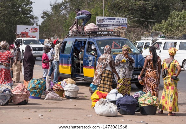Serekunda,\
The Gambia - june 23, 2019: Group of people with luggage waiting\
for minibuses in front of the animal\
market