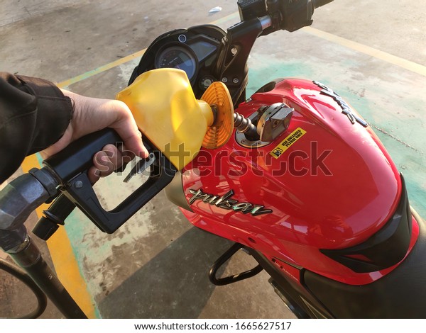 SEREMBAN, MALAYSIA -FEBRUARY 21, 2020: Petrol is\
being poured into the tank of a motorcycle using a yellow nozzle.\
Motorcycle using unleaded petrol.\
