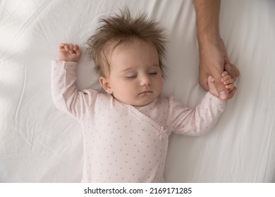 Serene adorable babygirl in pink bodysuit sleeping on bed holding tightly loving daddy thumb, touch finger feeling safety, close up above view. Family connection and ties, protection, cherish concept - Shutterstock ID 2169171285