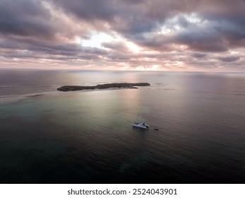 A serene aerial view of a sailboat anchored near a small island at sunset - Powered by Shutterstock