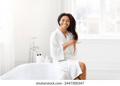 A serene African American woman combs her hair with a satisfied smile, in a clean and bright bathroom setting - Powered by Shutterstock