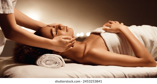 A serene African American woman lies on a spa bed receiving a gentle facial massage highlighting the concept of self-care and beauty - Powered by Shutterstock