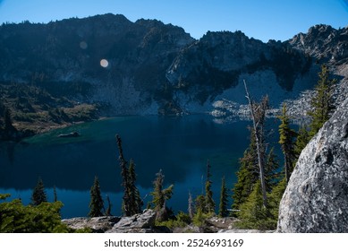 A serene alpine lake surrounded by rocky mountains and evergreen trees under a clear blue sky. The calm water reflects the mountainous landscape while various rock formations and forested areas add te - Powered by Shutterstock