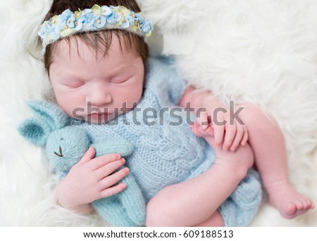 Serene baby girl all dressed in blue knitted costume with her bunny toy, closeup
